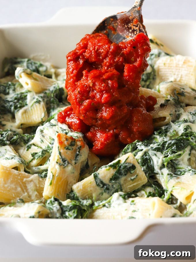 Pasta with spinach and ricotta being topped with easy tomato sauce ready to be baked.
