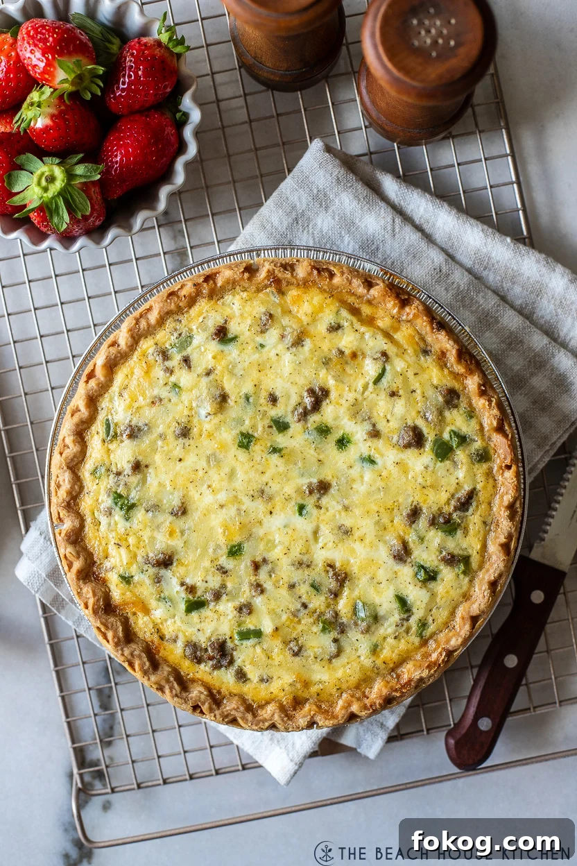 Up close overhead photo of a sausage pepper and onion quiche on a wire rack with a small bowl of strawberries