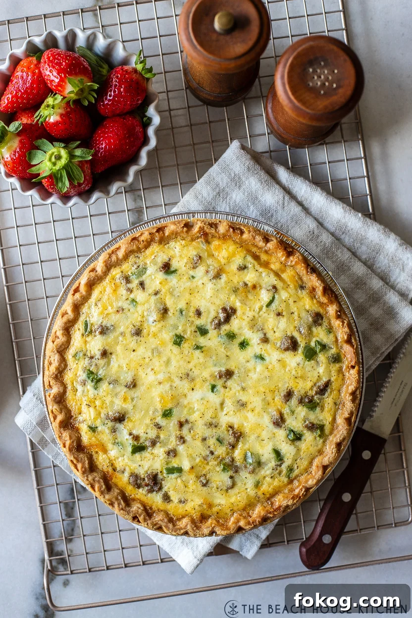 Overhead photo of a sausage pepper and onion quiche on a wire rack with a bowl of strawberries and wooden salt and pepper shakers