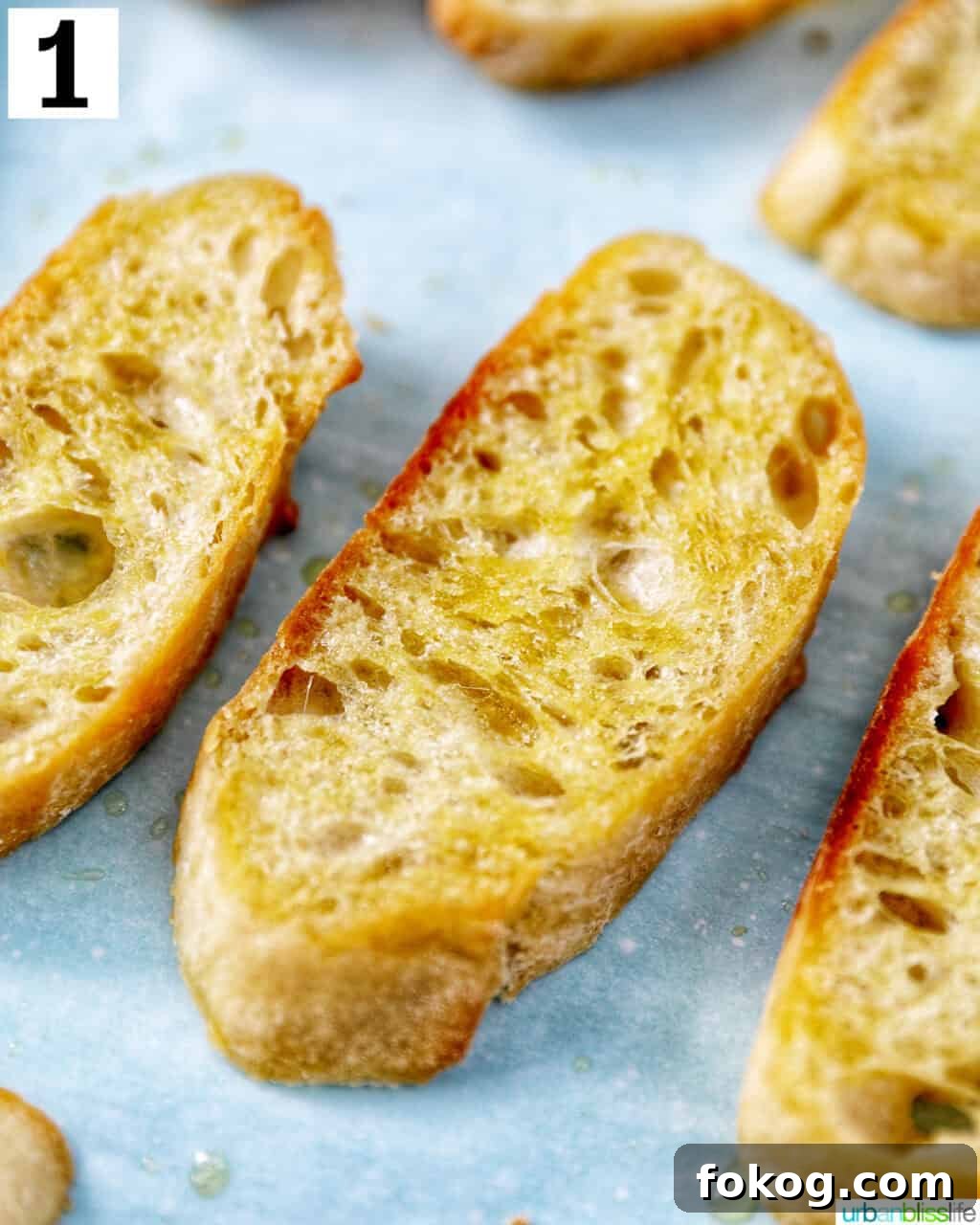 closeup of sliced baguette with olive oil on a baking sheet.