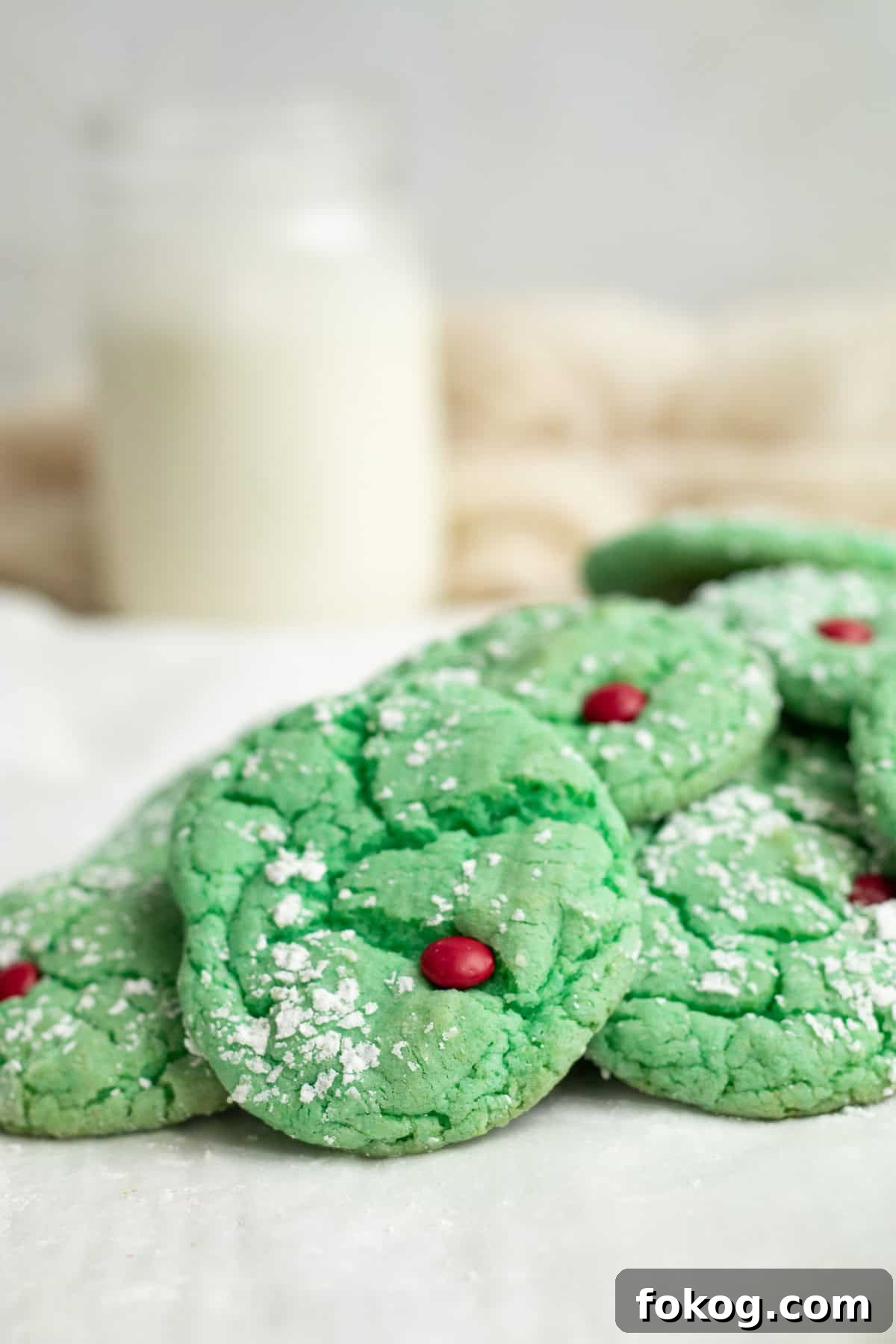 grinch cake mix cookies on parchment paper in a pile with a glass of milk