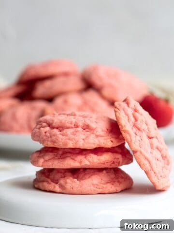 four strawberry cake mix cookies stacked on a white plate.