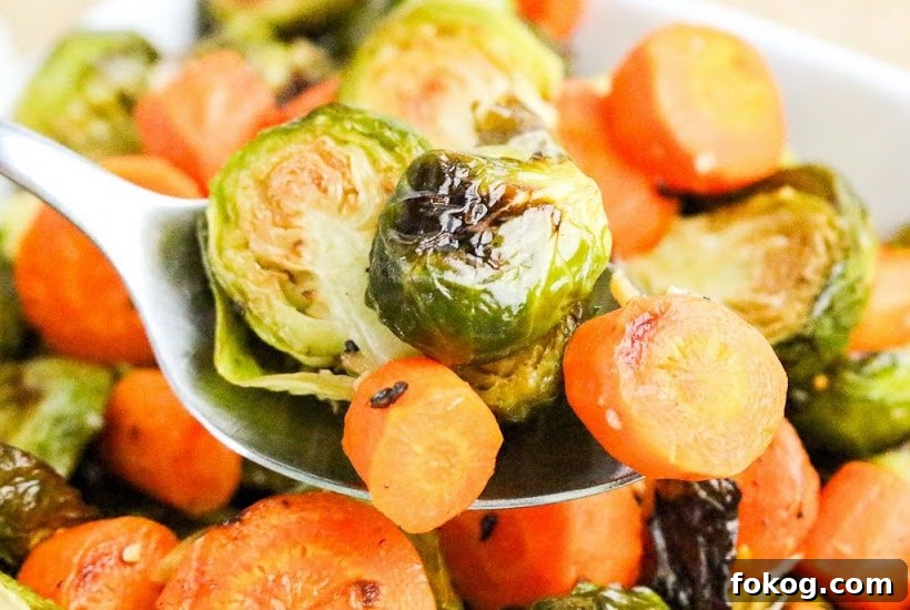 Crispy Roasted Brussels Sprouts with Honey-Glazed Carrots 5 Scooping out baked brussels sprouts and carrots from a bowl using a spoon.