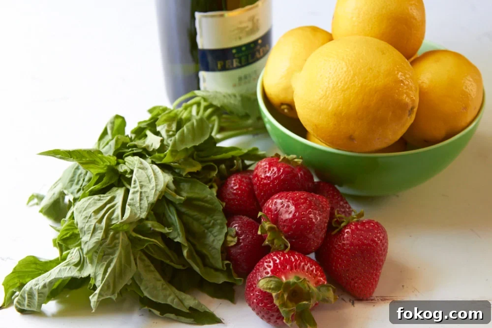 A bowl of lemons, some fresh strawberries, a bunch of fresh basil and a bottle of Prosecco on a white surface.
