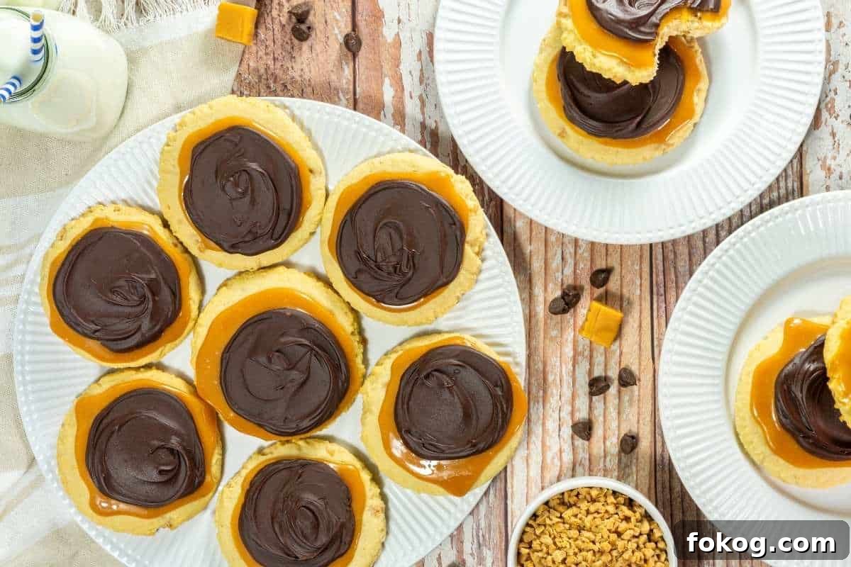 A plate of Copycat Crumbl Twix Cookies, with more cookies on separate plates, caramel pieces, and small chocolate chips nearby on a wooden table.