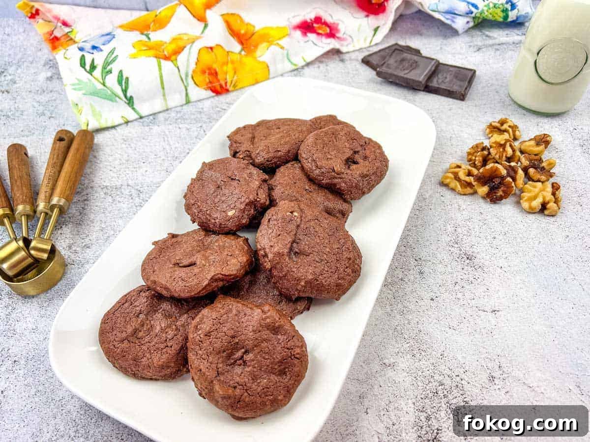 A plate of chocolate cookies with walnuts and chocolate pieces on the side.