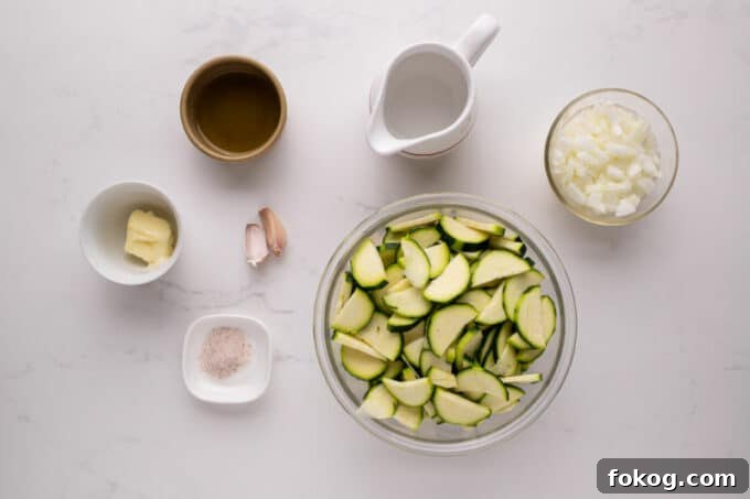 Zucchini, onion, garlic, and olive oil laid out on a table.