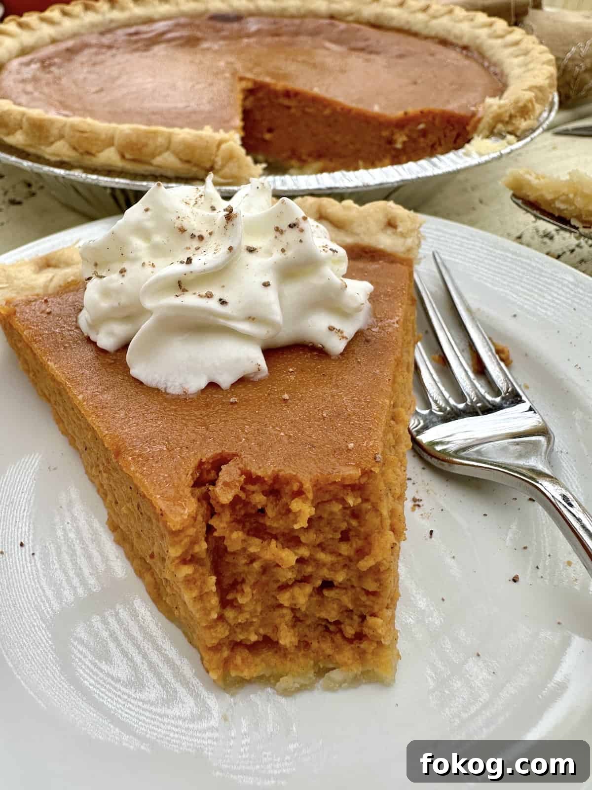 A slice of pumpkin pie with the pie in the background.