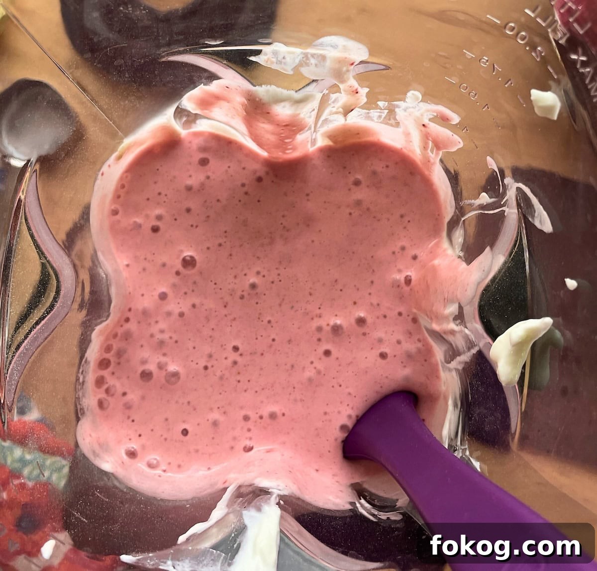 Strawberry Banana Yogurt Smoothie Recipe — Creamy & Refreshing 5 A blender with yogurt, strawberries, bananas, and milk blended up in it with a purple rubber spatula scraping down the sides.