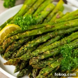 A plate of air fryer asparagus garnished with lemon and parsley.
