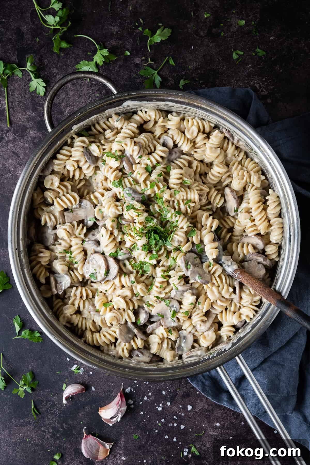 Creamy vegan mushroom pasta with truffle oil - this incredible vegan pasta is rich, creamy and delicious. With a cashew cream sauce and truffle oil it is an indulgent, comforting and impressive meal that is easy to make but tastes amazing! #veganmeal #dairyfree #plantbased A metal pan of creamy vegan mushroom pasta on a dark surface with fresh parsley and garlic skins.