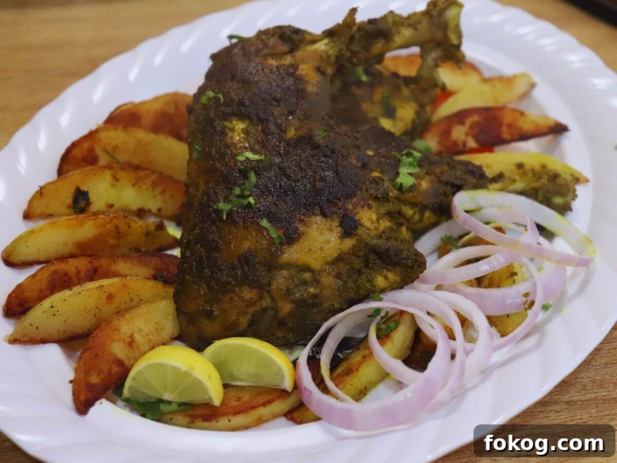 Goan Chicken Cafreal (Galinha Cafreal) Recipe — Authentic Flavor 2 close-up of chicken cafreal served in a white colored plate with roasted potato wedges, onion rings and lemon wedges.