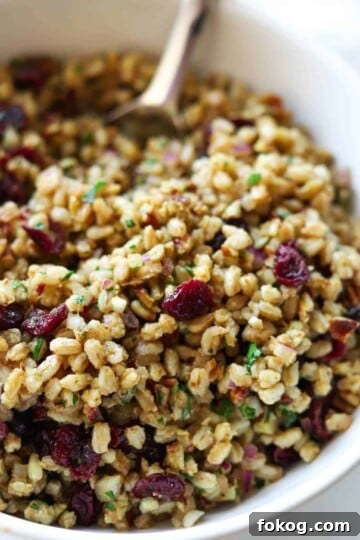 Farro salad in white bowl topped with pecans and cranberries.
