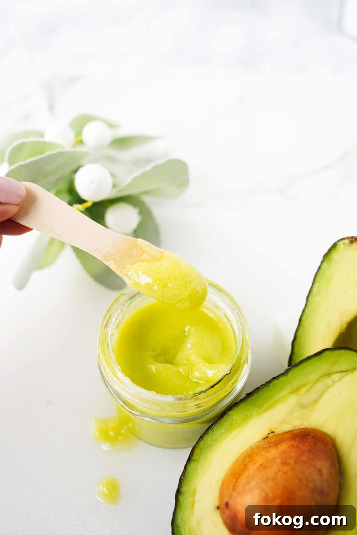 wooden spoon with avocado hand and face cream in small jelly jar with avocados next to the jar