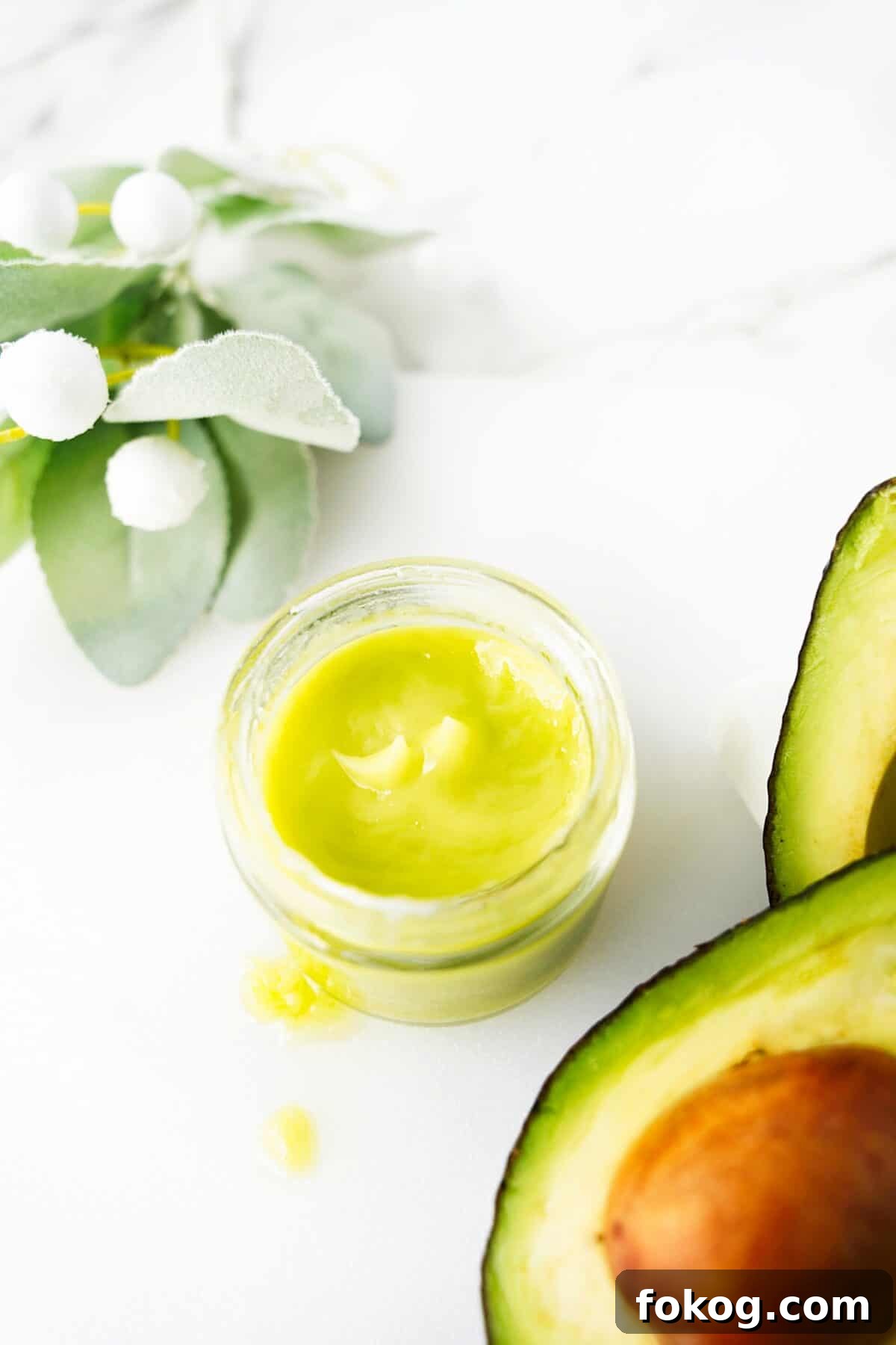 overhead shot of homemade avocado face and hand cream in jelly car with avocados cut open sitting on the side of the jar