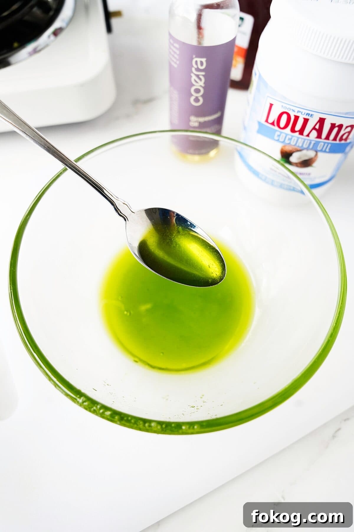 mashed avocados and oils and being strained in a glass bowl with spoon showing consistency