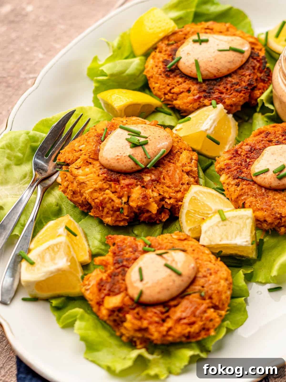 Tuna patties on a bed of lettuce surrounded by lemon wedges.