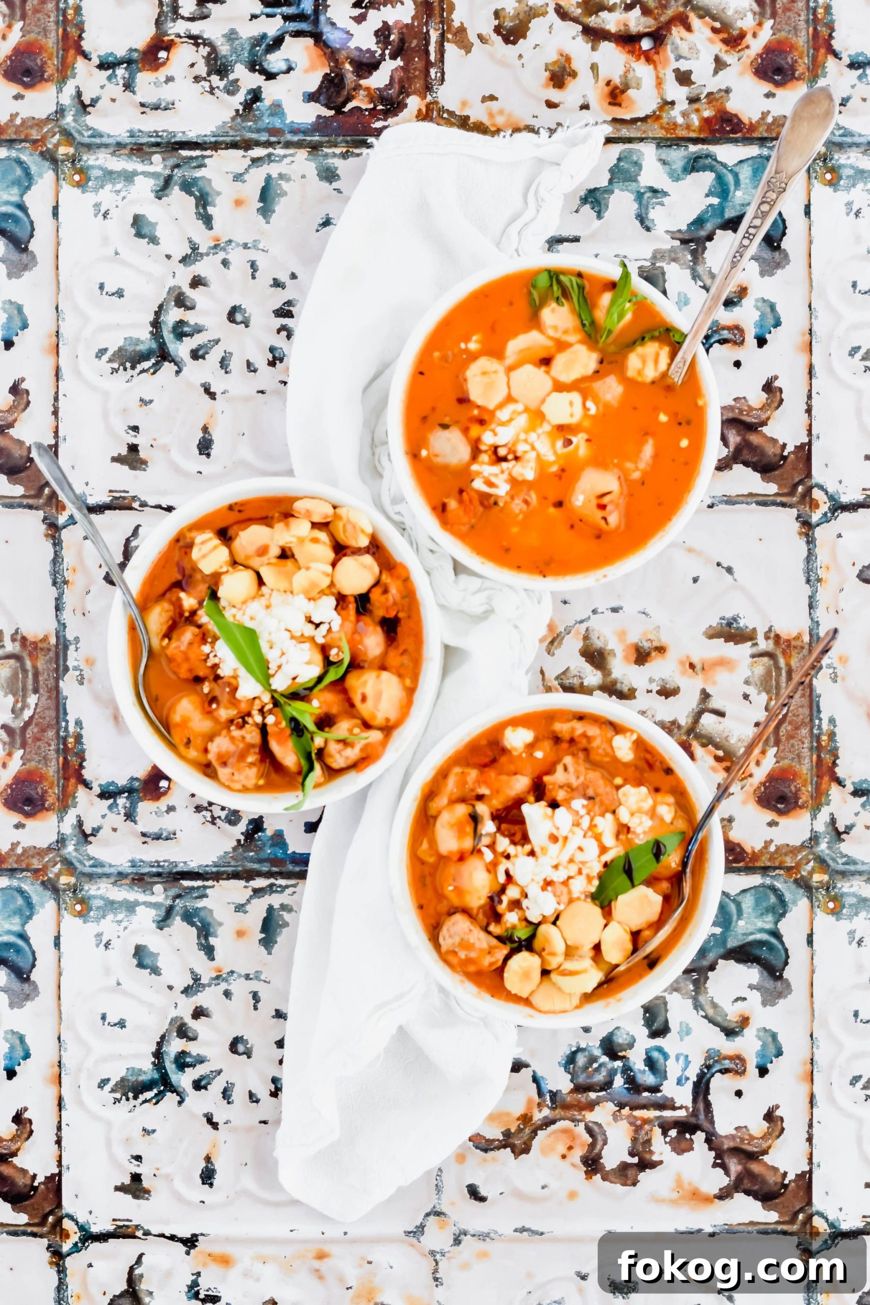 Three bowls of Cauliflower Gnocchi Soup with sausage garnished with oyster crackers on white linen.