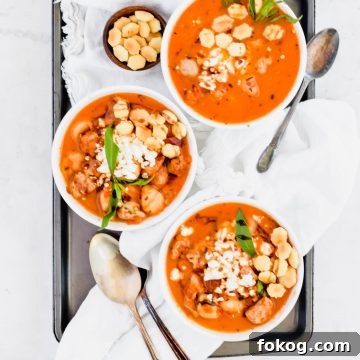 Three bowls of Cauliflower Gnocchi Soup with sausage garnished with oyster crackers on white linen.
