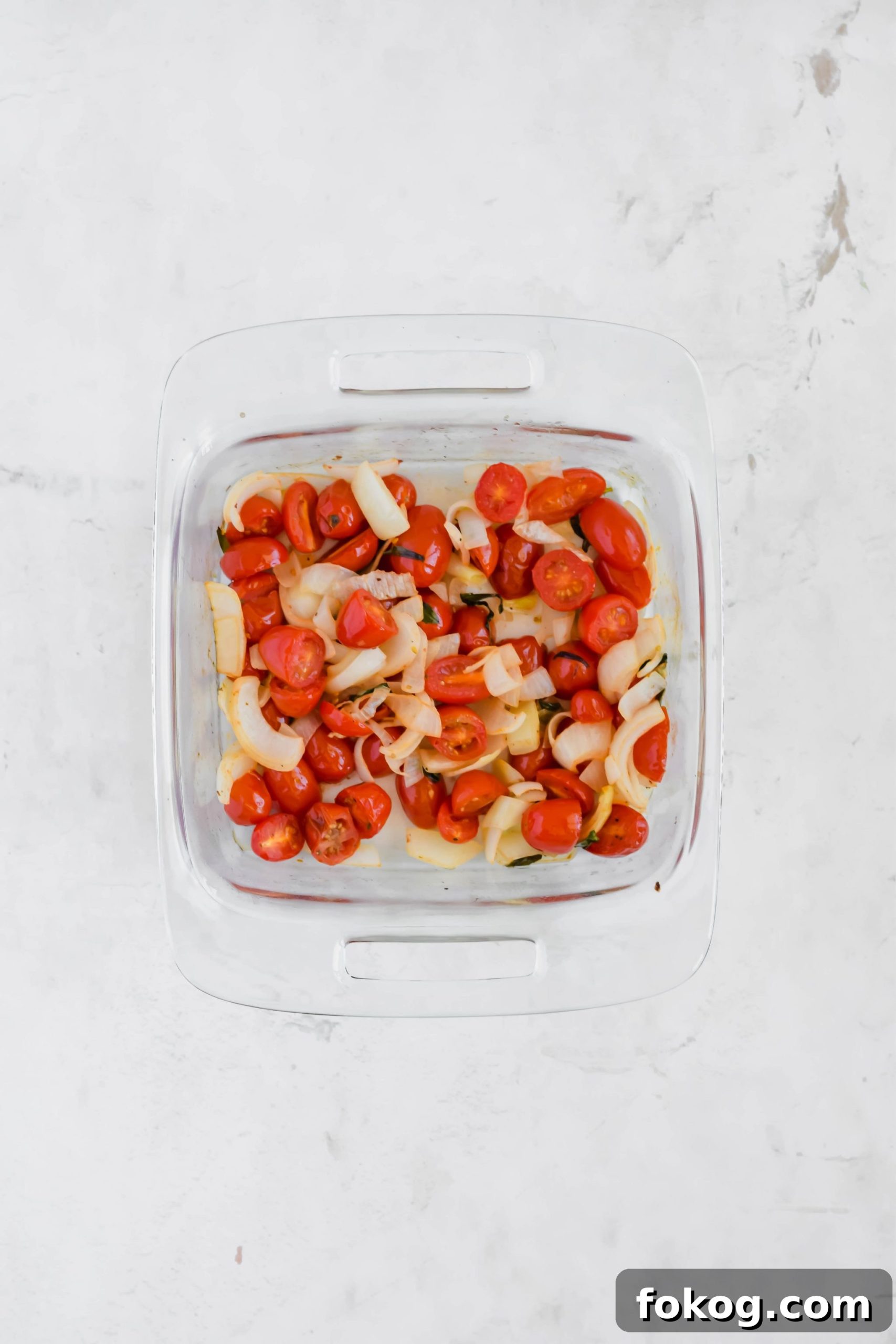 Roasted onion and tomatoes in a glass baking dish for Cauliflower Gnocchi Soup with sausage.