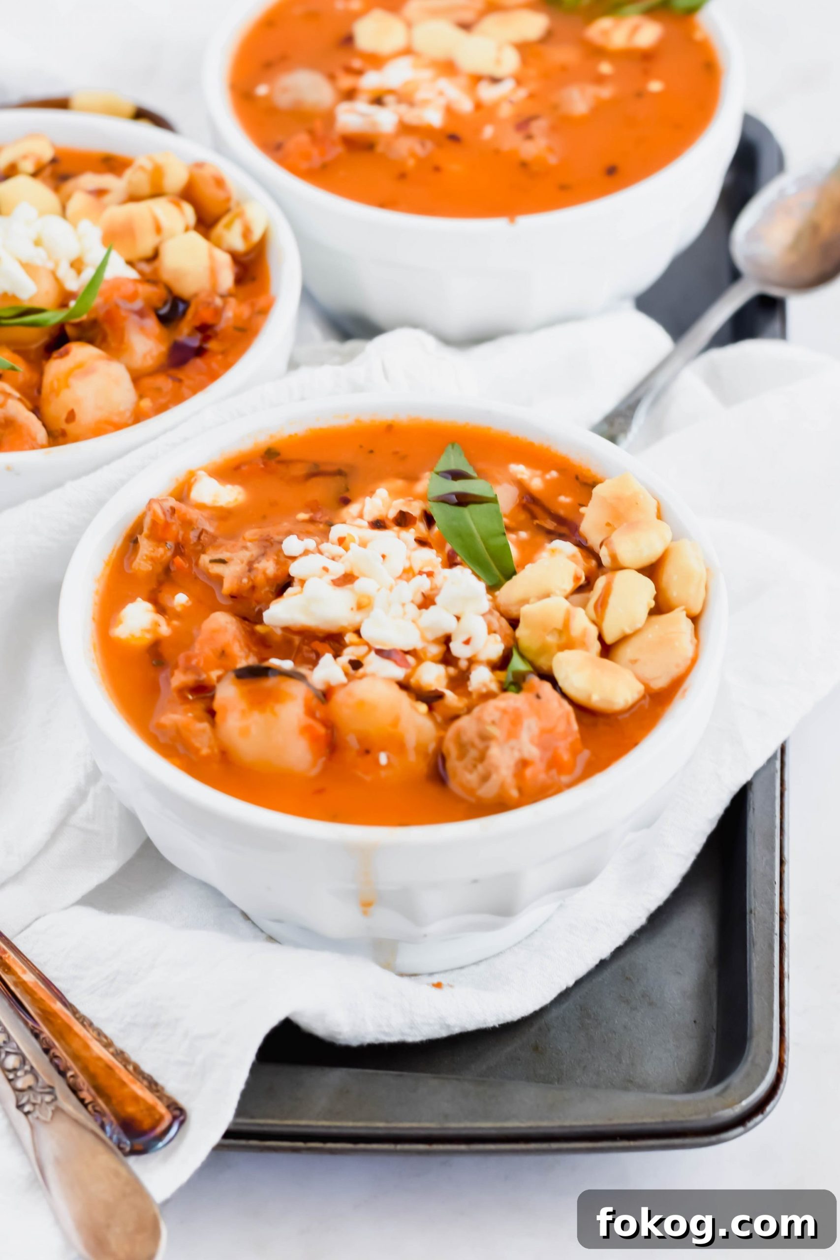 Three bowls of Cauliflower Gnocchi Soup with sausage garnished with oyster crackers on white linen.