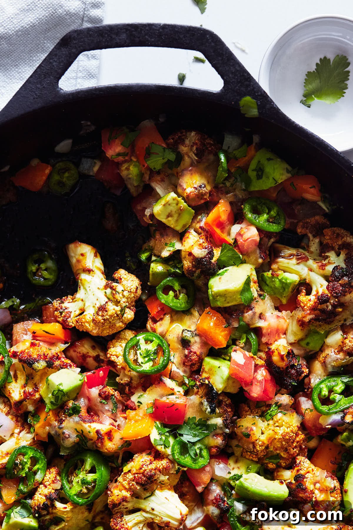 Spicy Cauliflower Nachos with Melted Cheese & Jalapeños 6 Close up of spiced cauliflower nachos in a cast iron pan with small amount scooped out