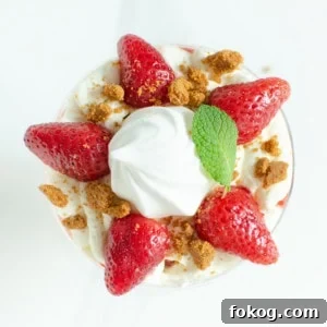 Crushed biscuit and mint leaf placed on top of the cream and strawberries in a glass to create our Eton mess dessert