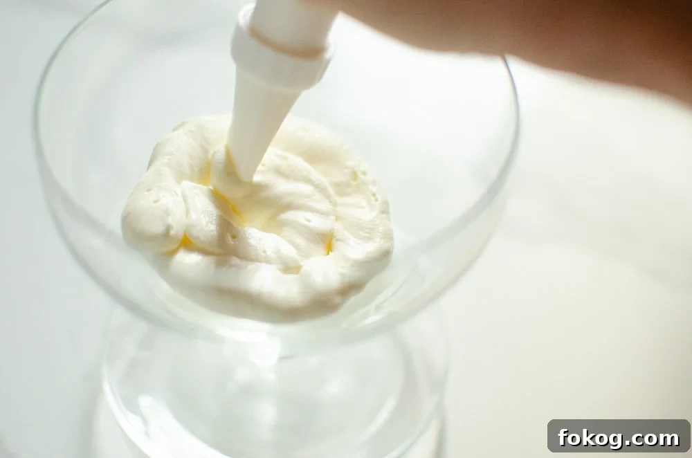 whipped cream being piped into a cold glass to make Eton mess dessert
