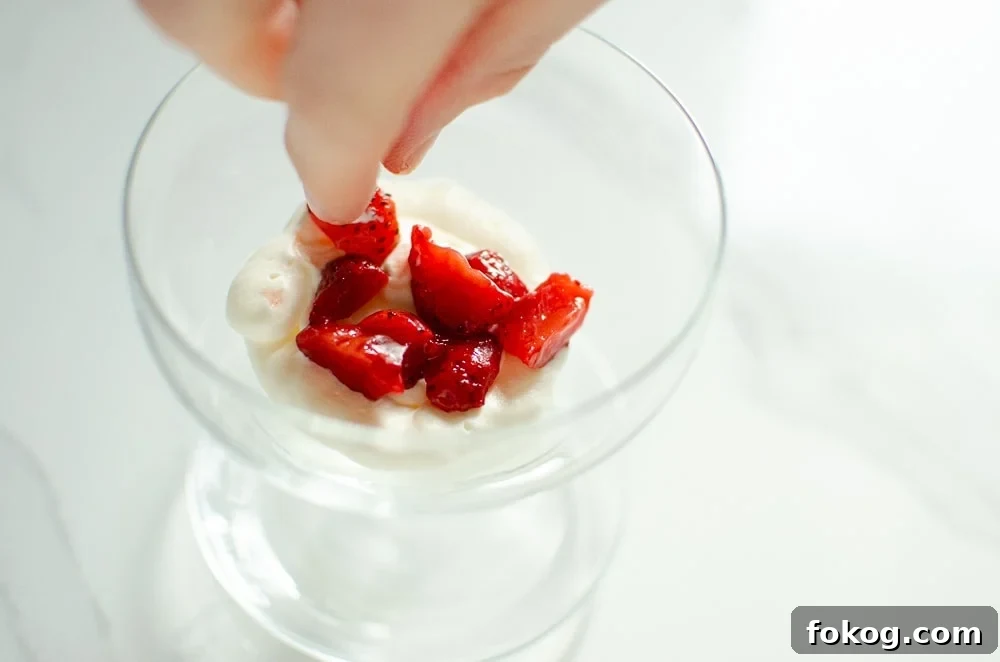 Chopped strawberries being placed on the whipped cream in a glass