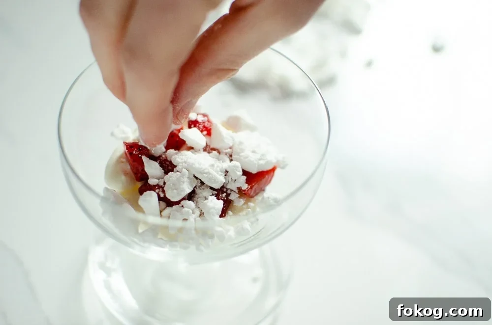 Crushed meringue being placed on top of the cream and strawberries to make Eton mess dessert