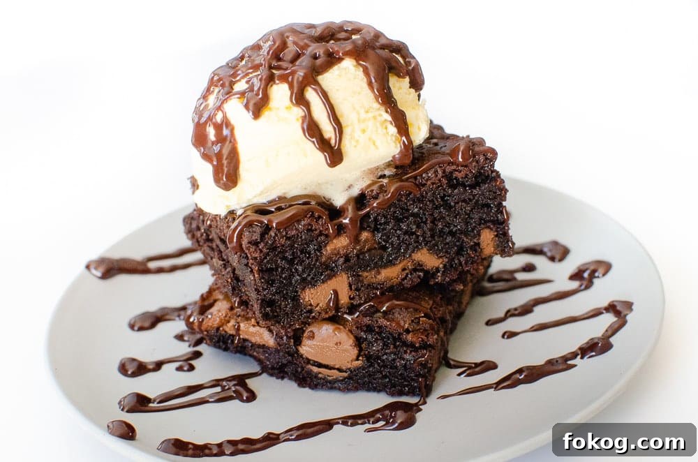 Chunky Chocolate Chip Brownies on a grey plate drizzled with chocolate sauce and vanilla ice cream on top