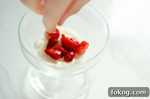 Chopped strawberries being placed on the whipped cream in a glass
