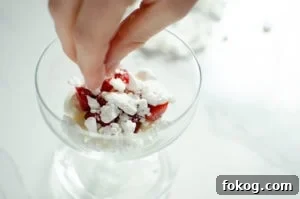 Crushed meringue being placed on top of the cream and strawberries to make Eton mess dessert