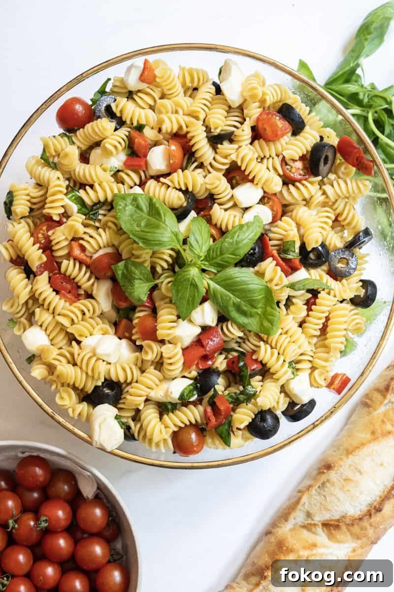 Classic Italian Pasta Salad Recipe with Tangy Vinaigrette and Veggies 2 Italian pasta salad in a large bowl with garnish of basil, on the side is a loaf of bread and bowl of cherry tomatoes.