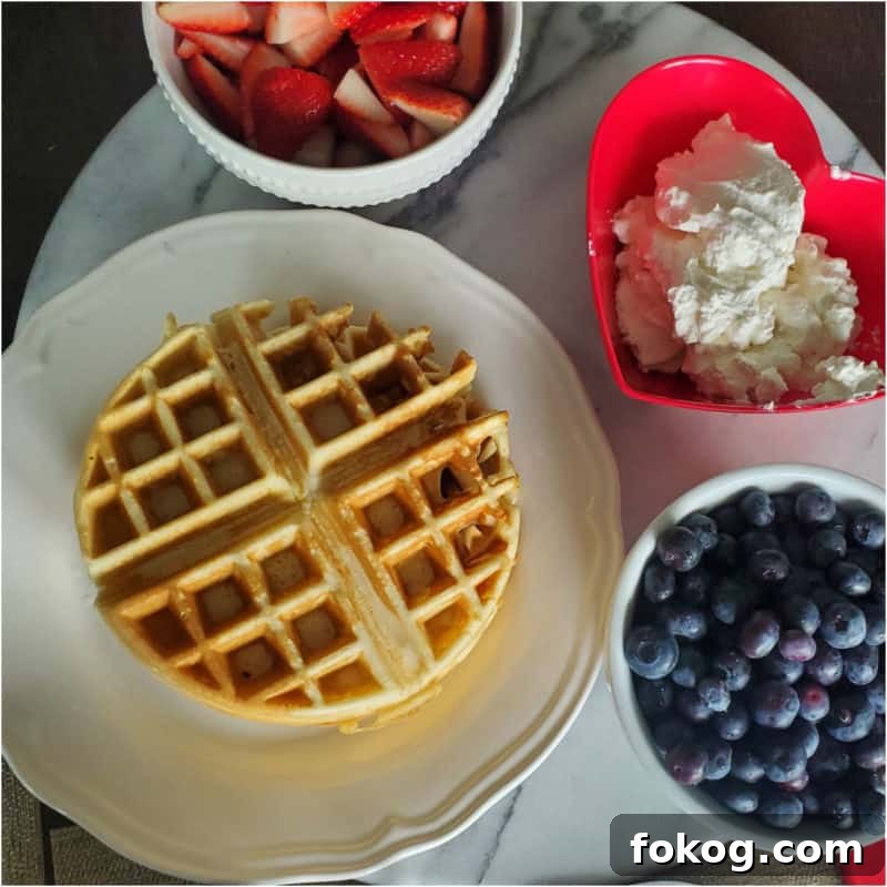 Simple Bisquick Recipes for Delicious Breakfasts and Snacks 5 Bisquick waffle on a white plate with strawberries, whipped cream, and a bowl of blueberries
