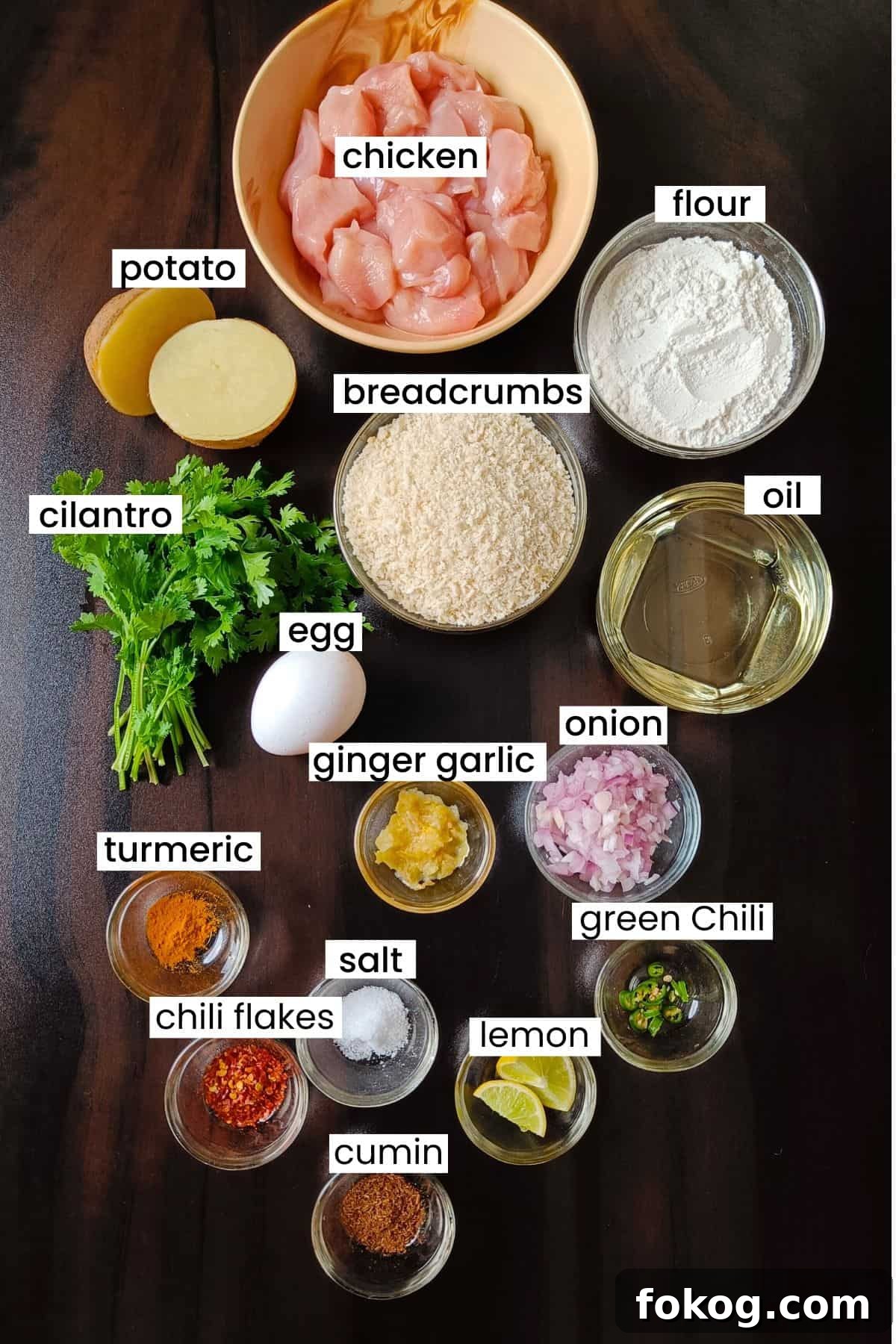 Ingredients for making chicken cutlets are placed on a dark brown background.