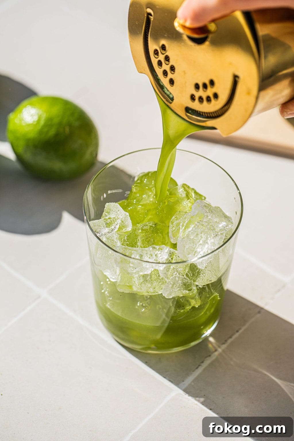 straining the matcha cocktail into an old fashioned glass over ice