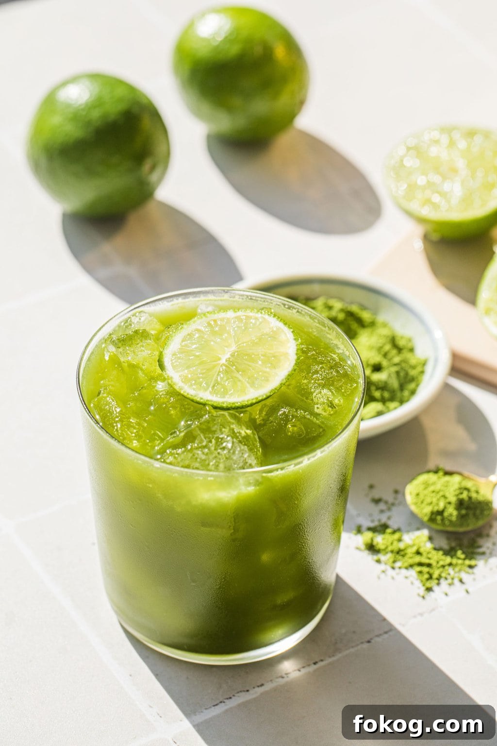 an old-fashioned glass full of a green margarita with a lime wedge on top for garnish, and match powder in the background