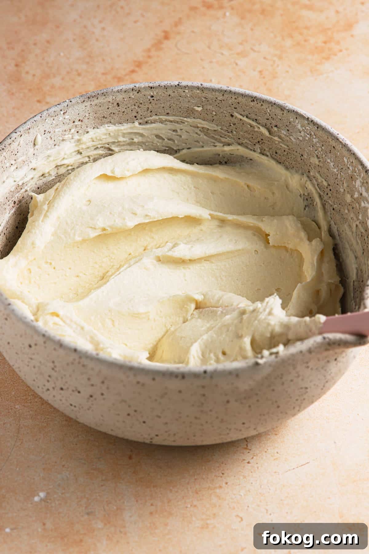 Mascarpone frosting in a bowl with a spatula.