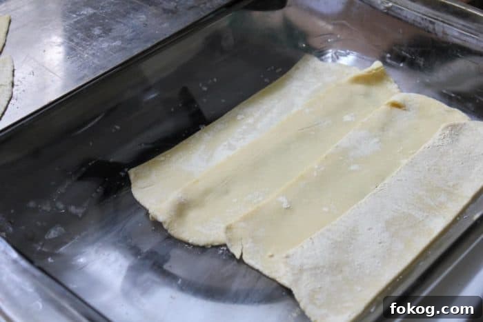 Image shows uncooked lasagna noodles placed in a pan