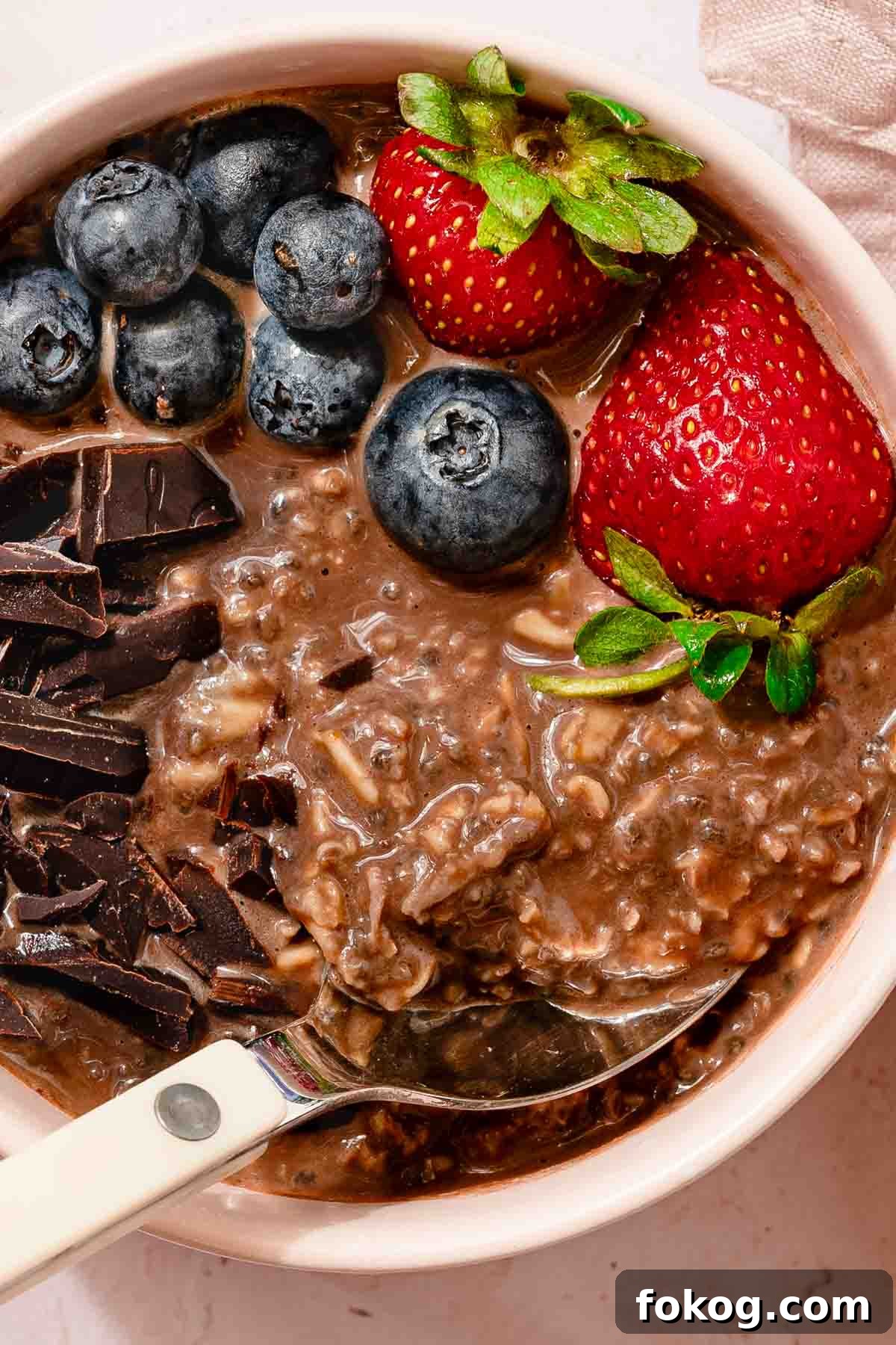 Creamy Chocolate Protein Overnight Oats 8 bowl of chocolate oatmeal with spoon chopped chocolate and fruit garnish.