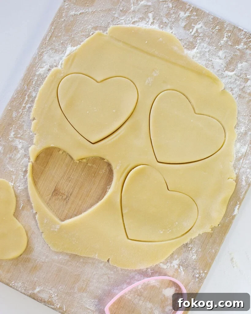 Sugar cookie dough rolled out into a thin layer on a wooden cutting board with heart shaped cutouts.