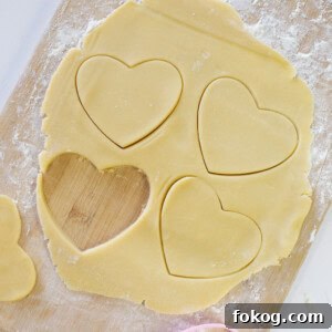 Sugar cookie dough rolled out into a thin layer on a wooden cutting board with heart shaped cutouts.