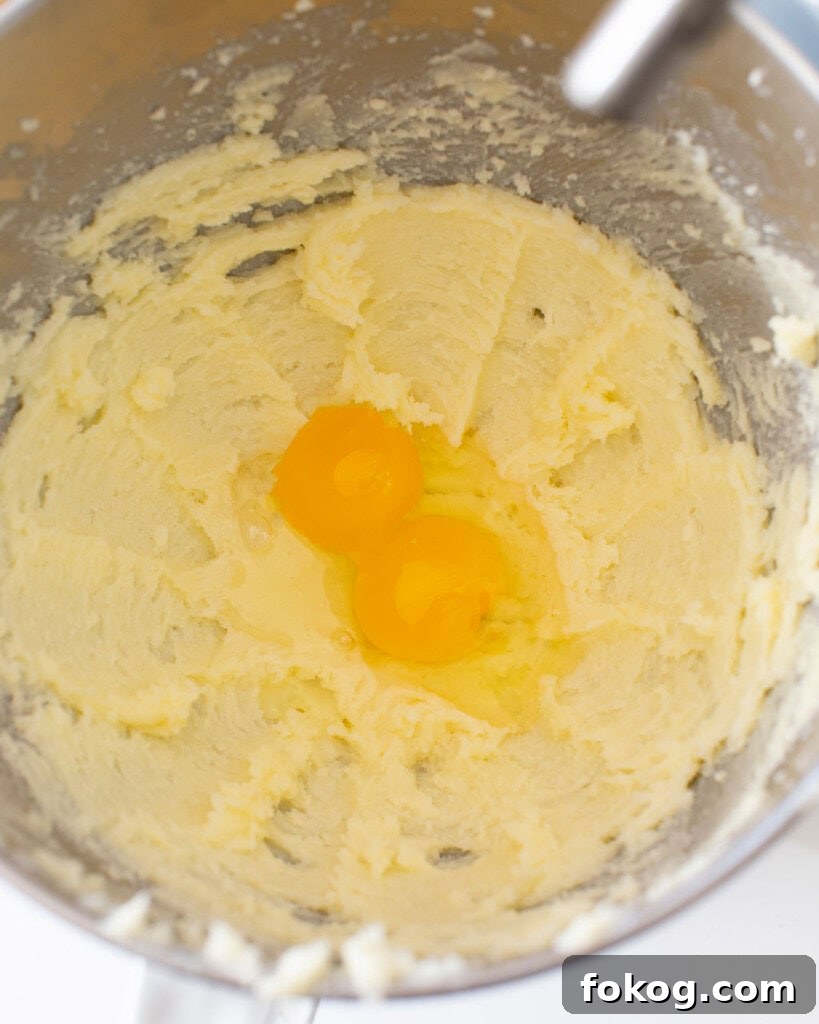 Butter and sugar mixture mixed with two raw eggs on top in a stand mixer bowl.
