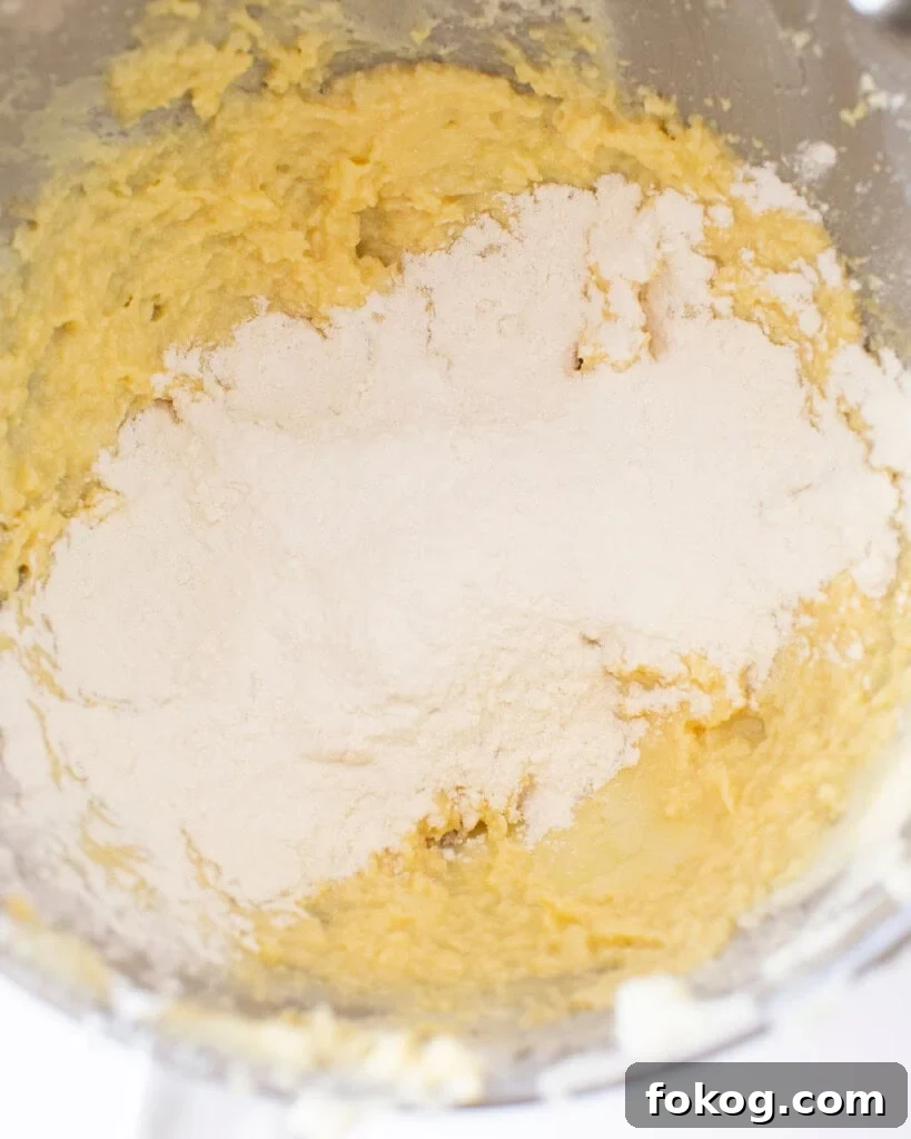 Butter, sugar, and egg mixture with flour on top in a stand mixer bowl.