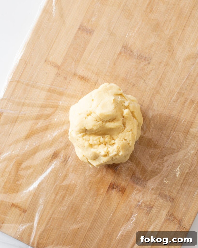 Sugar cookie dough rolled into a ball on top of plastic wrap on a cutting board.
