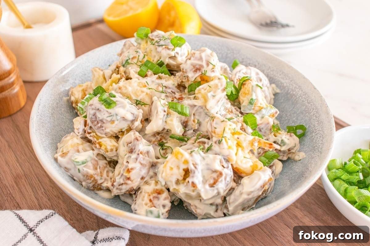 A bowl of smashed potato salad with creamy dressing, garnished with chopped green onions.