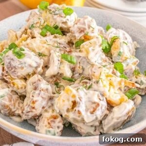 A bowl of smashed potato salad topped with chopped green onions rests on a wooden table.