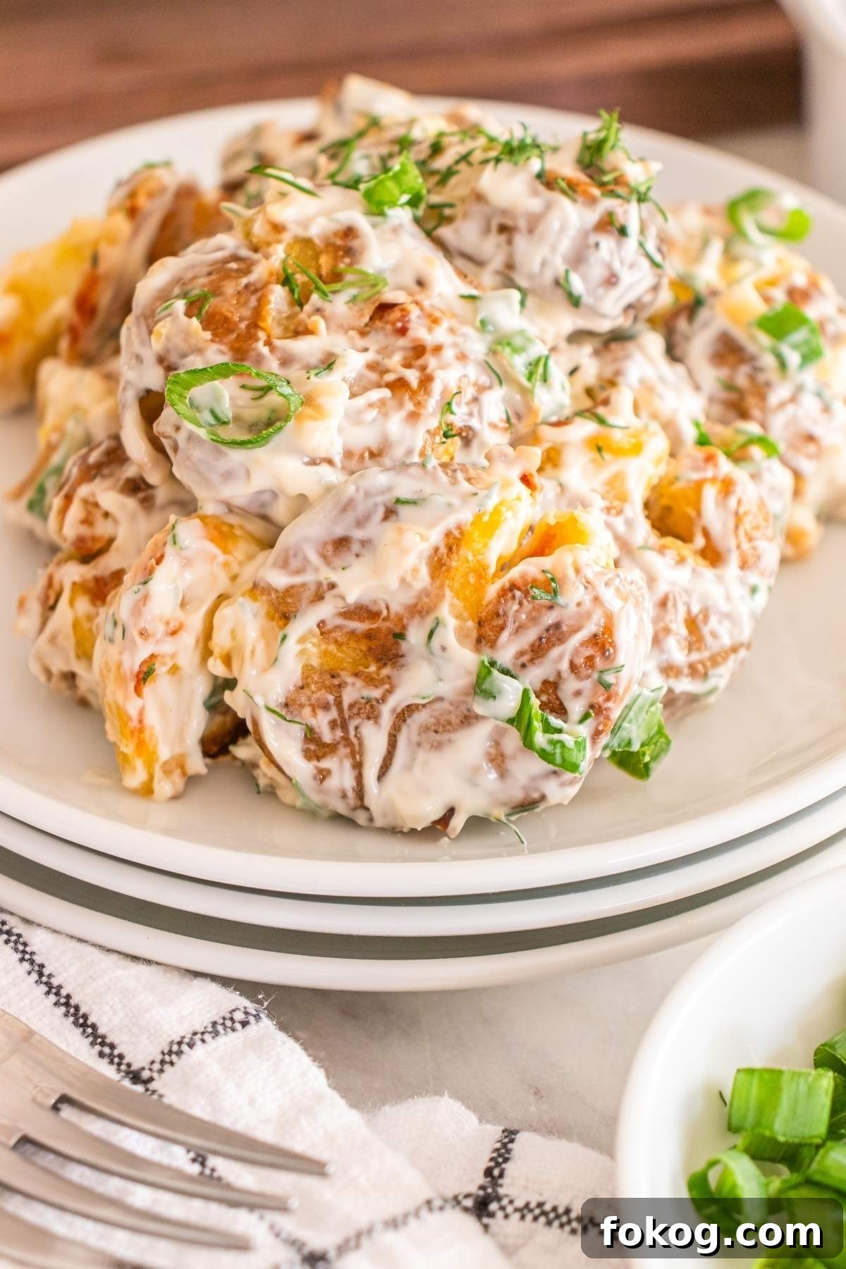 A plate of creamy smashed potato salad garnished with chopped green onions and dill.