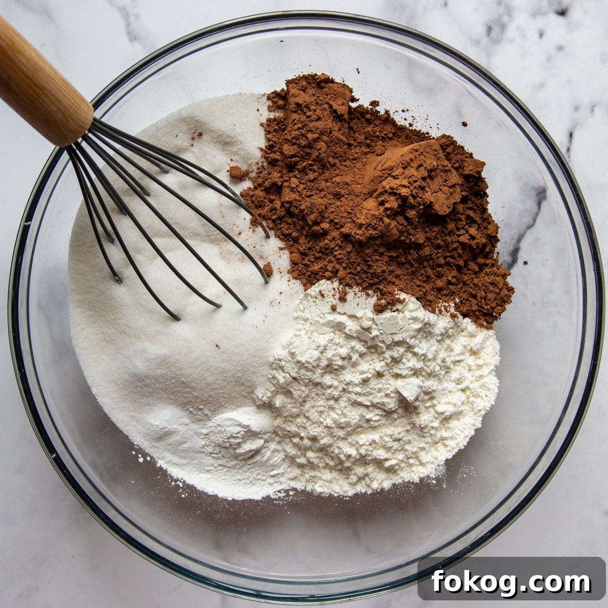 gluten free flour, sugar, cocoa, and other dry ingredients being whisked together in a large glass bowl.